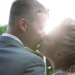Couple in wedding attire kissing with sunlight in background