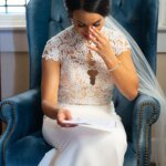 A St Louis Wedding Photographer captures a bride sitting in a chair, immersed in reading her heartfelt wedding vows.