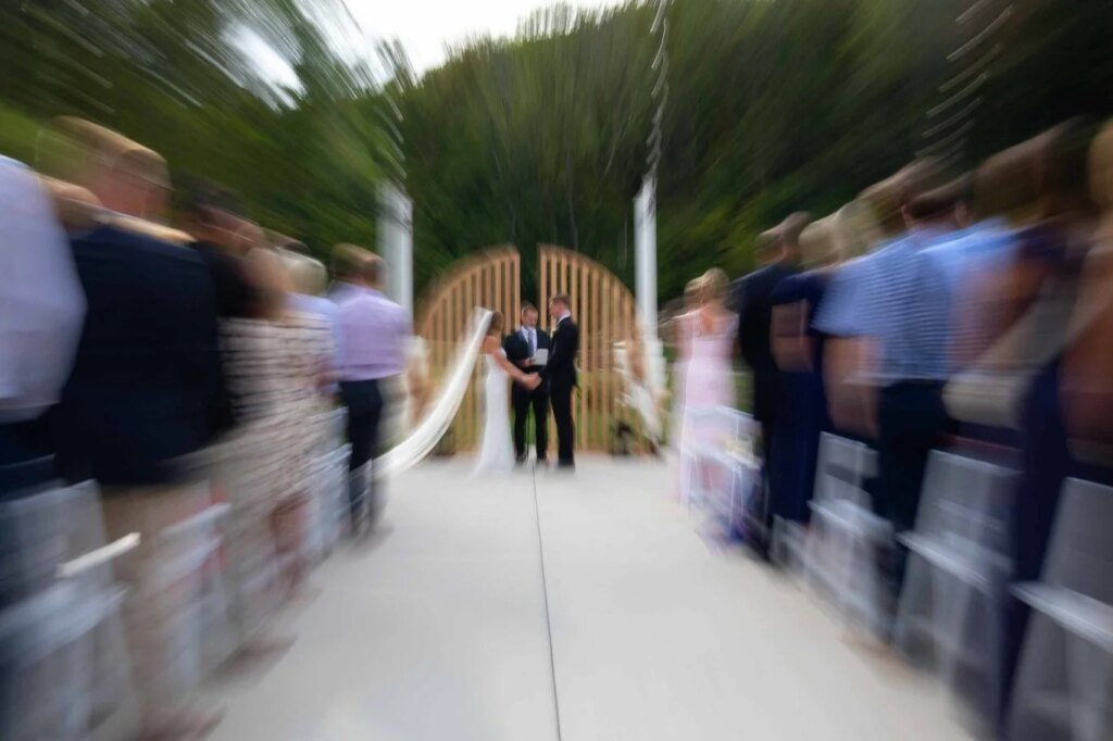 A couple stands at the altar during an outdoor wedding ceremony, captured beautifully through the lens of a wedding photographer, with blurred guests seated on either side.